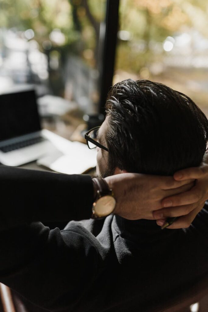A man takes a break, sitting back with hands behind head in an office.